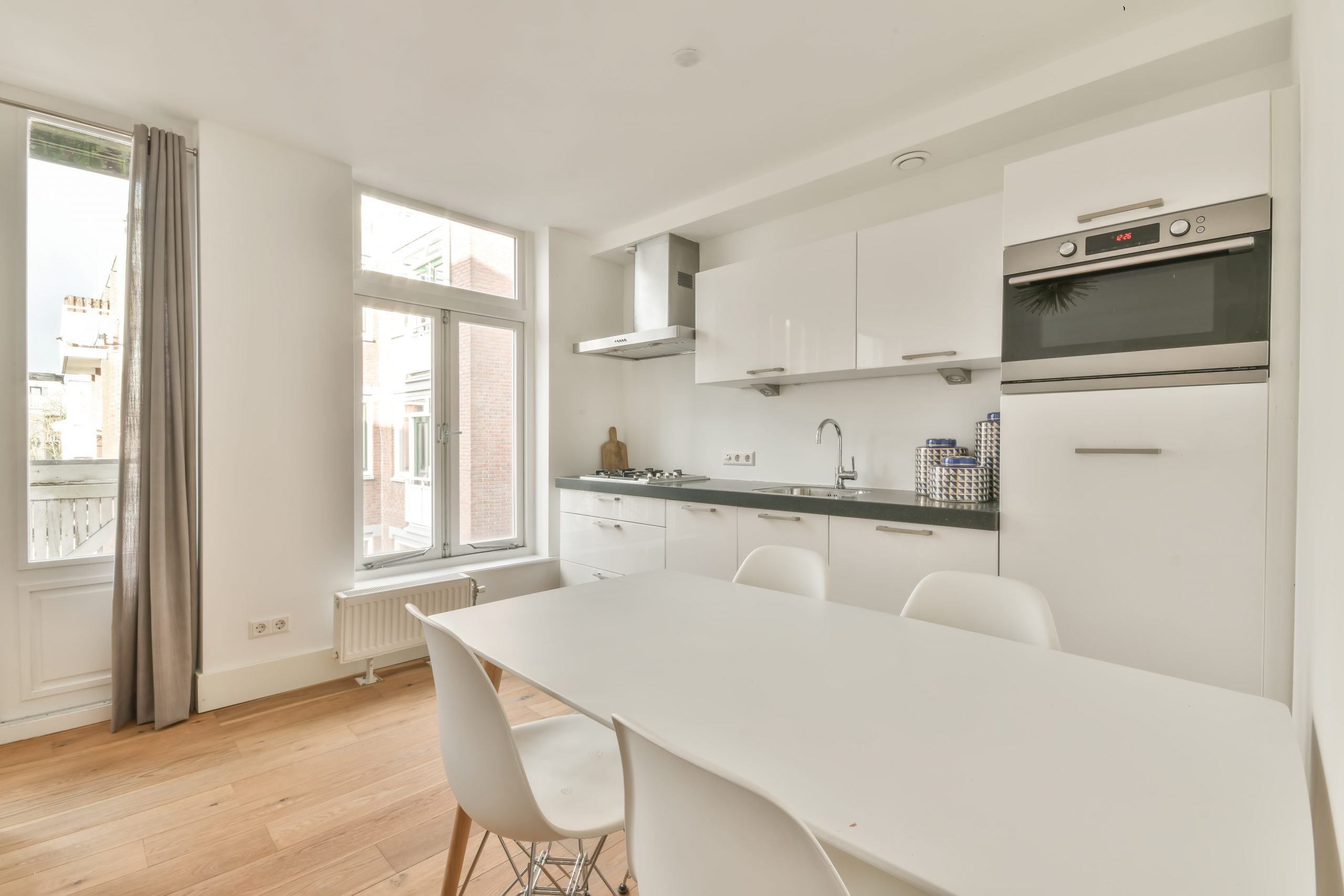 The interior of a modern apartment with a kitchen and dining area in white on a parquet floor